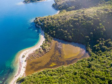 Bereketli yeşil tepeler ve okyanus arasında uzanan tenha bir kıyı lagününün havadan görünüşü..