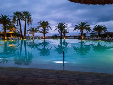 Suyu yansıtan palmiye ağaçlarıyla dolu bir tatil köyünde sakin bir akşam..