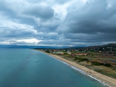 Dramatik bulutlar altında kıyı manzarası, sakin plaj sakin denizle buluşur.