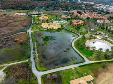 Su basmış bir gölet ve bereketli bir peyzaj yakınındaki tatil köylerinin havadan manzarası..