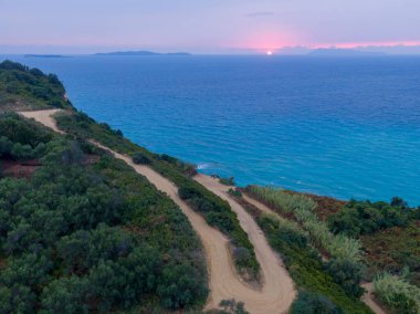 Kıyı günbatımı manzarası, turkuaz denizin üzerindeki dolambaçlı yol..