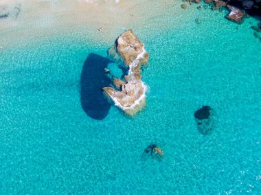 Kristal berraklığında turkuaz suda kayalık bir çıkıntının havadan görünüşü.