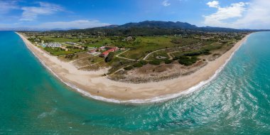 Turkuaz bir deniz boyunca yeşil ve dağlarla desteklenen tenha bir sahil manzarası..