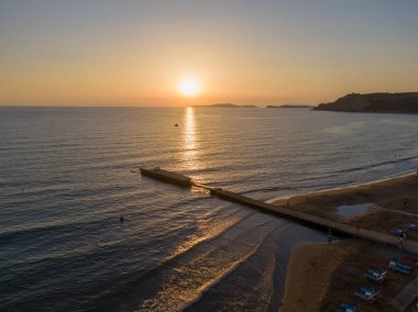 Sakin okyanusun üzerinde gün batımı, kumsala uzanan iskele..