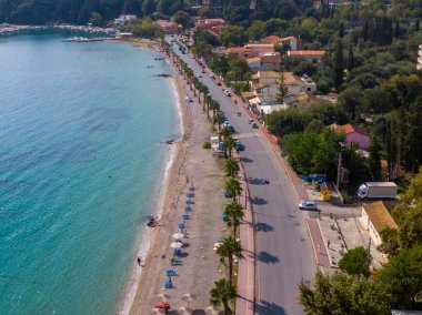 Sahil yolu boyunca turkuvaz suyu ve palmiye ağaçları olan bir sahil..