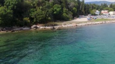 Canlı, mavi yüzen bir rıhtım, sakin, turkuaz bir suya, ağaçlarla kaplı bir sahilin arka planına ve uzaktaki küçük bir köye uzanıyor. Temiz su, denizin dibini ortaya çıkarır., 