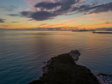 Kıyı burnu üzerinde gün batımı ve sakin deniz. Sakin, renkli gökyüzü.