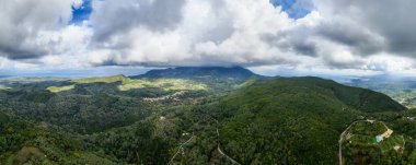 Bulutlu bir gökyüzünün altındaki yemyeşil dağların panoramik manzarası. Huzurlu manzara.