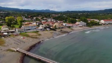 Yunanistan 'ın Korfu adasındaki Roda turist kasabası. Renkli evleri, plaj barları, restoranları, güneşli yatakları, şemsiyeleri ve turkuaz suyu olan deniz kıyısındaki güzel bir köy. Drone görünümü