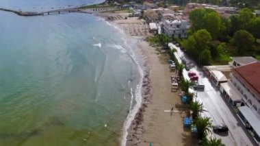 Yunanistan 'ın Korfu adasındaki Roda turist kasabası. Renkli evleri, plaj barları, restoranları, güneşli yatakları, şemsiyeleri ve turkuaz suyu olan deniz kıyısındaki güzel bir köy. Drone görünümü