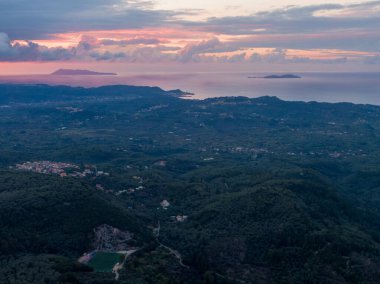 Dağlar, ormanlar ve deniz manzaralı sakin bir manzaranın üzerinde gün batımı görüntüsü..