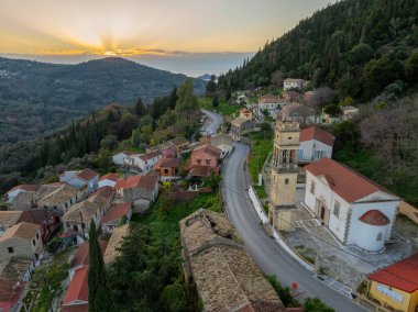 Terracotta çatıları ve kilisesi olan büyüleyici bir yamaç köyünün üzerinde gün batımı..