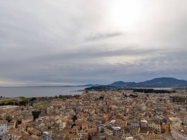 Yukarıdan deniz manzaralı, bulutlu bir gökyüzünün altında. Binalar ve deniz görünür..