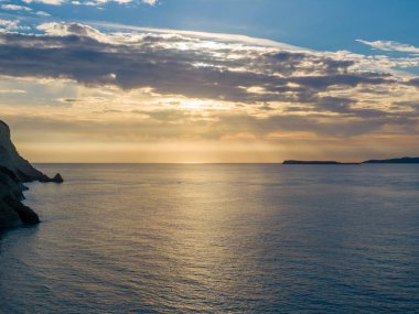 Uzak adaları ve kayalıkları olan sakin okyanusun üzerinde altın gün batımı