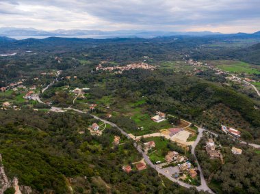 Bereketli yeşilliklerin ve dolambaçlı yolların arasına kurulmuş sakin bir sahil köyünün havadan görünüşü.