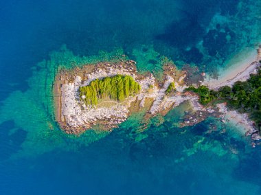 Turkuaz sudaki küçük bir adanın havadan görünüşü. Bereketli yeşil bitki örtüsü beyaz kayalar ve berrak denizle çelişiyor..