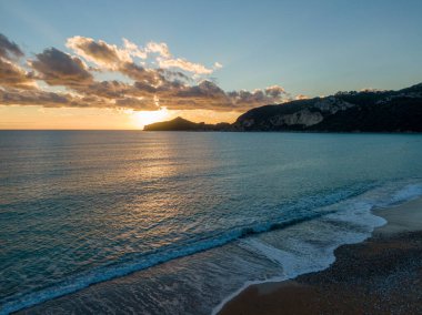 Sakin bir okyanusta gün batımı, dalgalar yavaşça kıyıya vuruyor..