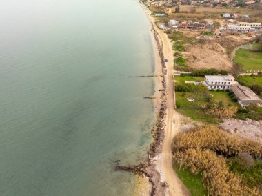 Sakin bir hava perspektifi, kara ve denizin buluşmasını yakalar. Sakin sular, kayalar ve yeşilliklerle kaplı kumlu bir kıyıya çarpar. Sahil bitki örtüsü ve binalar dingin atmosfere katkı sağlıyor..