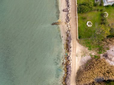Kayalar, kumlar ve bitkilerle dolu sakin bir kıyı şeridinin havadan görünüşü.