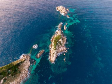 Okyanustaki temiz turkuaz suyla çevrili küçük bir adanın havadan görüntüsü..