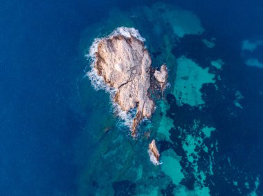 Canlı mavi okyanus sularında kayalık bir adanın havadan görünüşü.