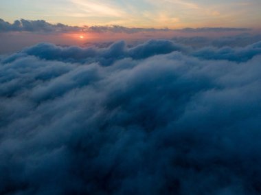 Bulutların üzerinden gün batımı manzarası, sıcak renklerle gökyüzünü boyuyor..
