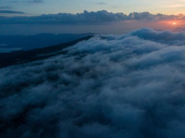 Bulutların üzerinde gün batımı, uzaktaki dağlar..