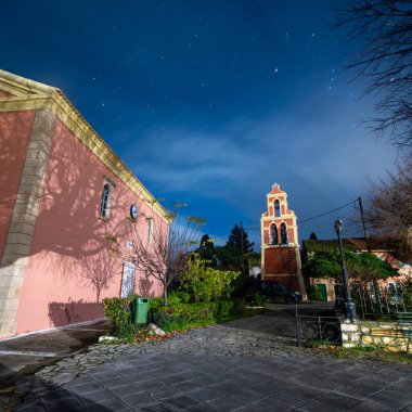 Yıldızlı gökyüzünün altında bir kilise ve çan kulesinin gece sahnesi.