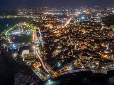 Mimarisini ve limanını gözler önüne seren, aydınlatılmış bir sahil şehrinin gece görüşü.