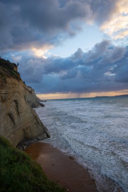 Dramatik sahil kayalıkları düşüncelere dalmış gökyüzünün altında dalgalı bir denizle karşılaşıyor..