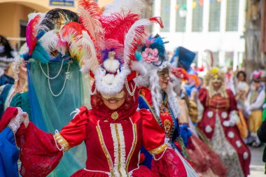Karnaval kostümleri ve maskeleri renkli giyimli insanlarla dolu canlı bir açık hava etkinliğinde sergileniyor..