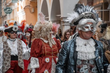Şenlikli bir atmosferde kutlama yapan şık kostümlü figürlerle dolu canlı bir sokak geçidi..