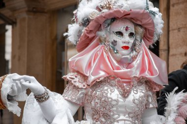 Gösterişli bir maskeli balo katılımcısı. Pembe ve beyaz bir kostüm ve mücevherlerle süslenmiş..
