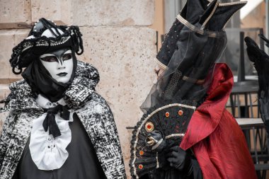 Özenle hazırlanmış maskeli ve kostümlü figürler bir şenlik ya da geçit törenine hazır olarak taşın önünde dururlar..