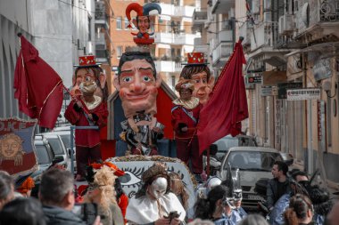 Büyük karakter başlıkları ve kırmızı bayraklarla kostüm giymiş insanların katıldığı festival geçidi..