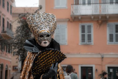Özenle hazırlanmış bir maske ve kostüm giymiş biri binanın önünde duruyor..