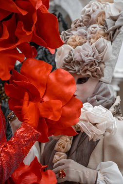 Büyük kırmızı çiçeklerle süslenmiş maskeli bir figür çarpıcı bir görsel ekran oluşturuyor.