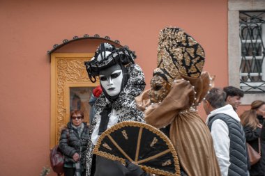 Kostümlü ve maskeli iki kişi şeftali renkli bir binanın önünde dikiliyorlar..