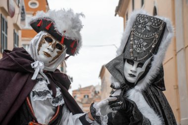İki özenle hazırlanmış figür, geleneksel kıyafetlerini ve maskelerini sergileyerek birbirlerine yakın dururlar..