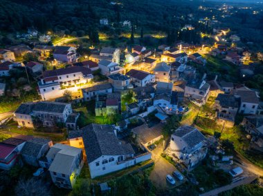 Sıcak ışıkları olan, evleri aydınlatan ve dolambaçlı yolları olan bir yamaçtan gece manzarası..