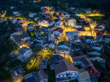 Alacakaranlıkta bir vadiye kurulmuş, binalardaki sıcak ışıklarla aydınlatılmış bir köyün havadan görünüşü..