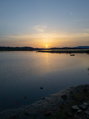 Altın gün batımı, sakin suyun üzerine sıcak bir parıltı saçar. Huzurlu ve güzel bir manzara yaratır..
