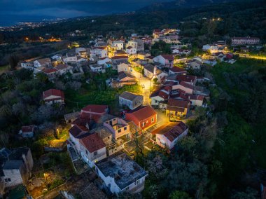 Aydınlanmış evler ve manzarayı noktalayan yeşilliklerle dolu bir köyün gece hava görüntüsü. Huzur.