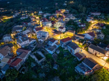 Hava manzarası, alacakaranlıkta hafif sokak lambalarıyla aydınlatılmış bir yamaçtaki köyün sessiz cazibesini yakalıyor..