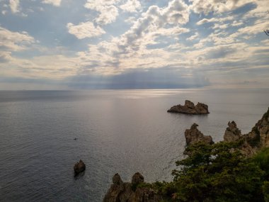 Kayalık uçurumlar, açık okyanus ve dokulu bulutlarla dolu dinamik bir gökyüzü içeren sakin bir deniz manzarası..