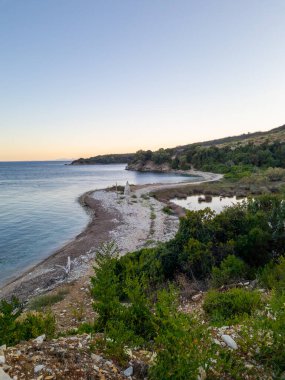Kıyı sükuneti: Kayalık bir sahil Pastel bir gündoğumu altında sakin denizle buluşur, yakınlarda yemyeşil yemyeşil.