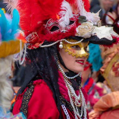 Korfu, korfu, Yunanistan. 02 Mart 2025: Venedik Karnavalı 'na katılan altın maskeli ve büyük tüylü şapkalı kırmızı kostümlü bir kadın.