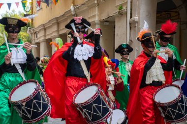 Canlı kostümler içindeki katılımcılar bir geçit töreninde davul, maske ve şapkalarla geçit töreni düzenliyorlar..