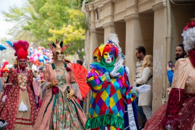 Gösterişli kostümler ve maskeler içinde bir grup insan bir geçit törenine ya da festival etkinliğine katılıyor..