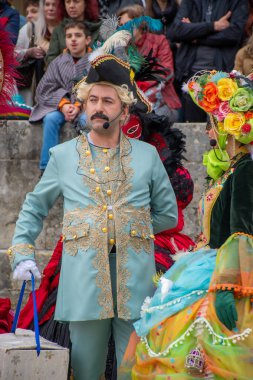 Süslü kostümlü, fırfırlı şapkalı, pudralı peruklu, mikrofonlu bir sanatçı..